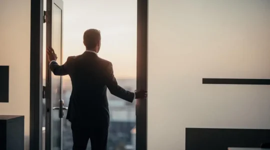Une personne se tient face à une porte entrouverte laissant filtrer une lumière chaude, symbolisant le passage vers une opportunité professionnelle intimidante